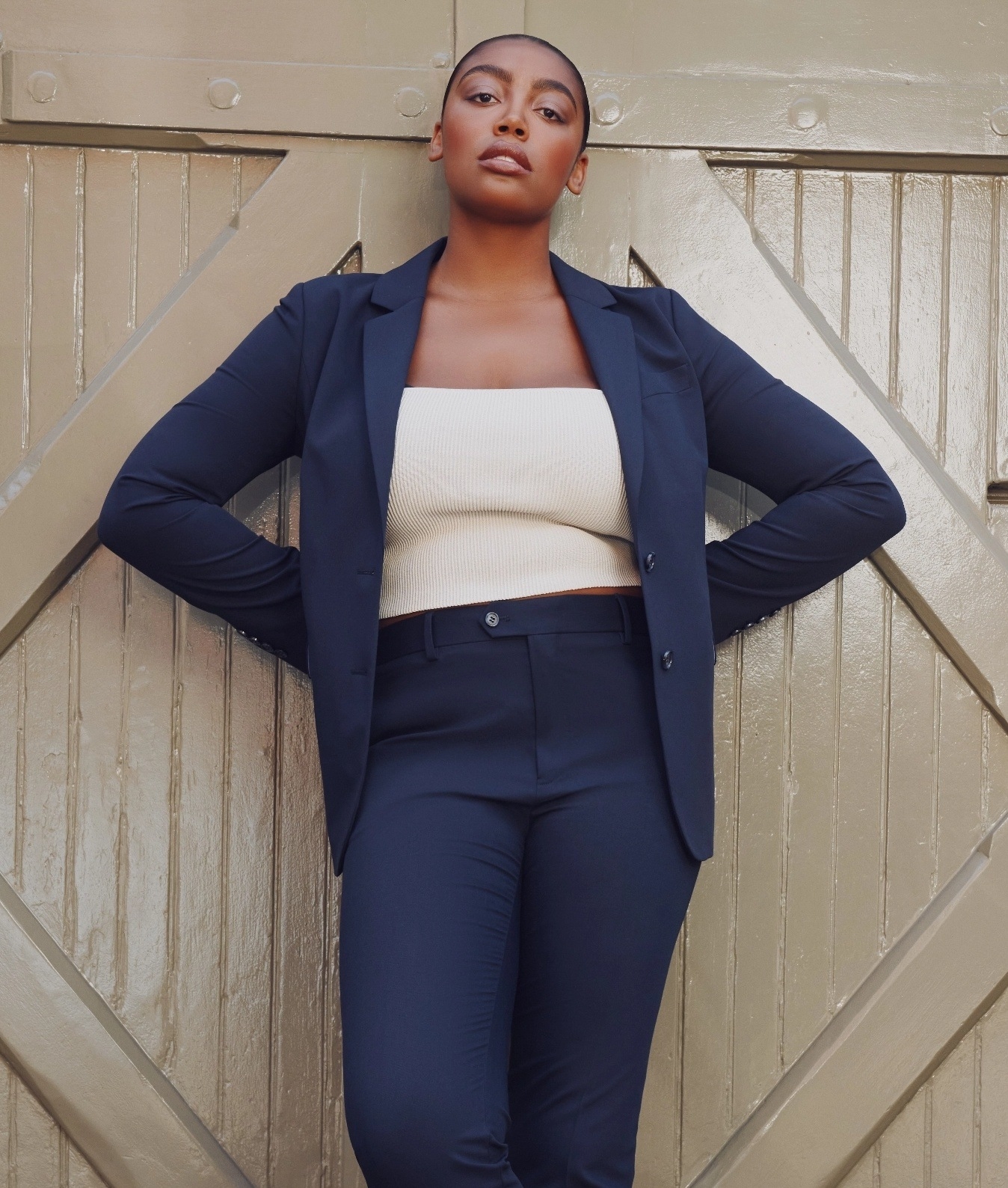 A woman stands outside wearing SuiShop navy suit, the jacket unbuttoned to show the pant waistline.
