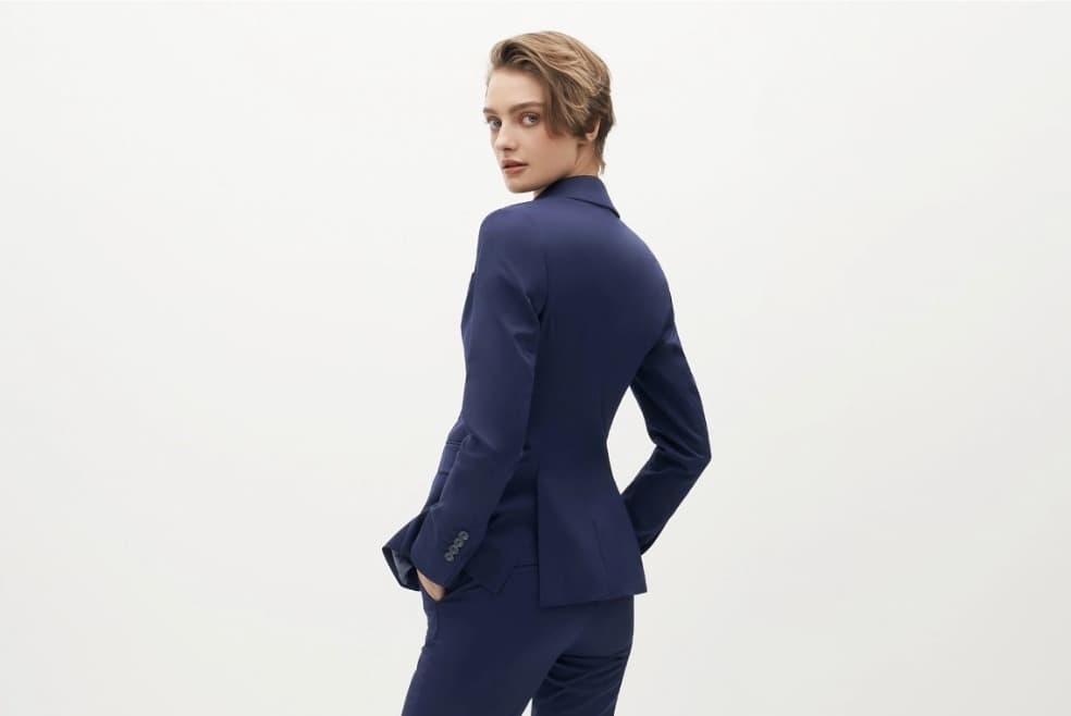 A woman in a navy suit faces away from the camera, showing the lack of tack stitches on the back of her jacket.