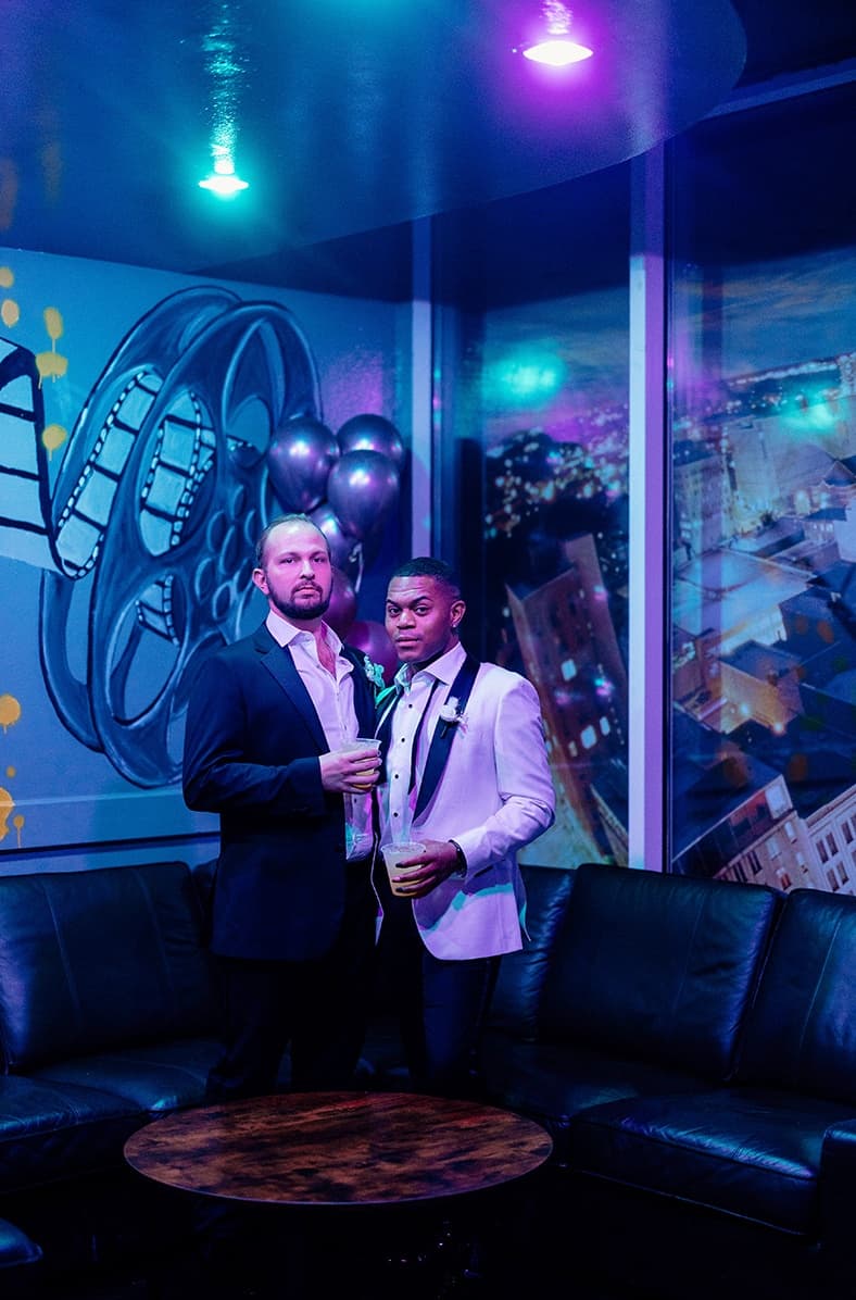 Styled shoot with two men in tuxedos and moody lighting.