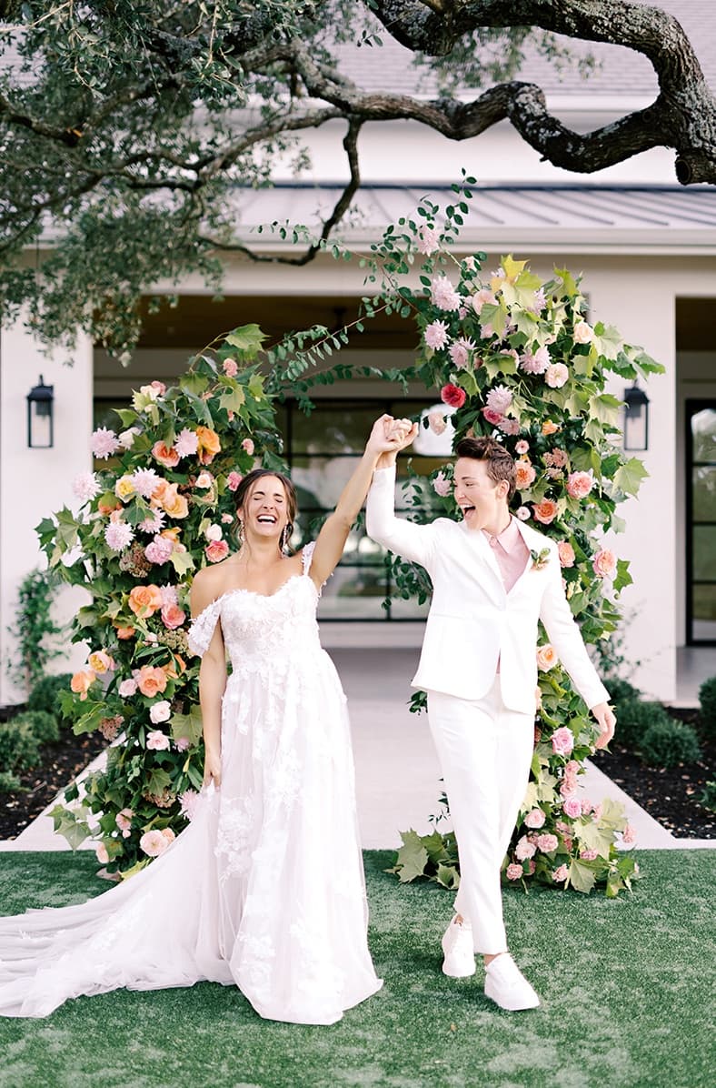 LGBTQIA+ wedding with two brides—one bride in soft wedding gown, another in a women's white tuxedo.