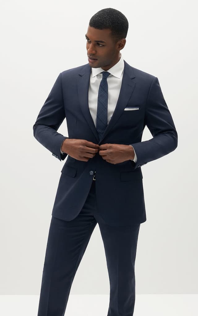 Man buttoning navy blue suit jacket wearing a matching navy tie.