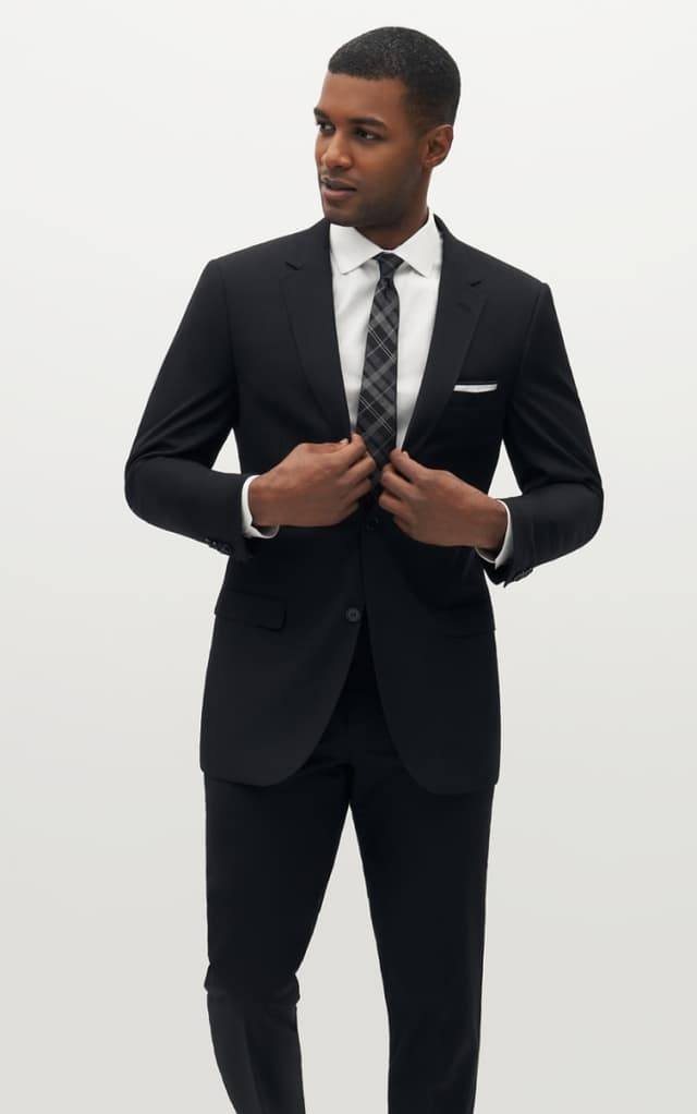 Man buttoning black suit jacket wearing a matching black tie.